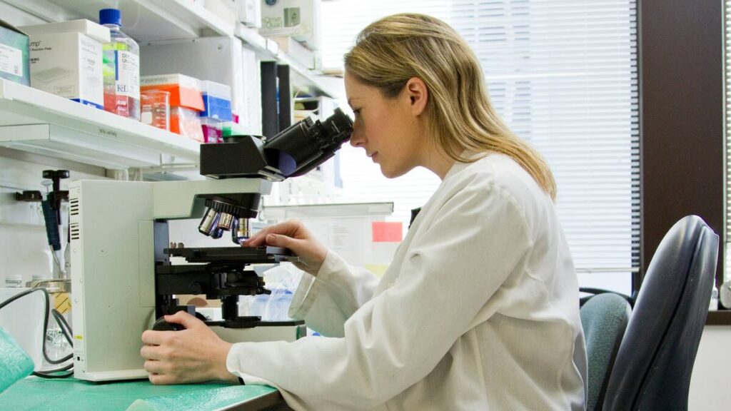 A peptide synthesis lab technician looks into a microscope